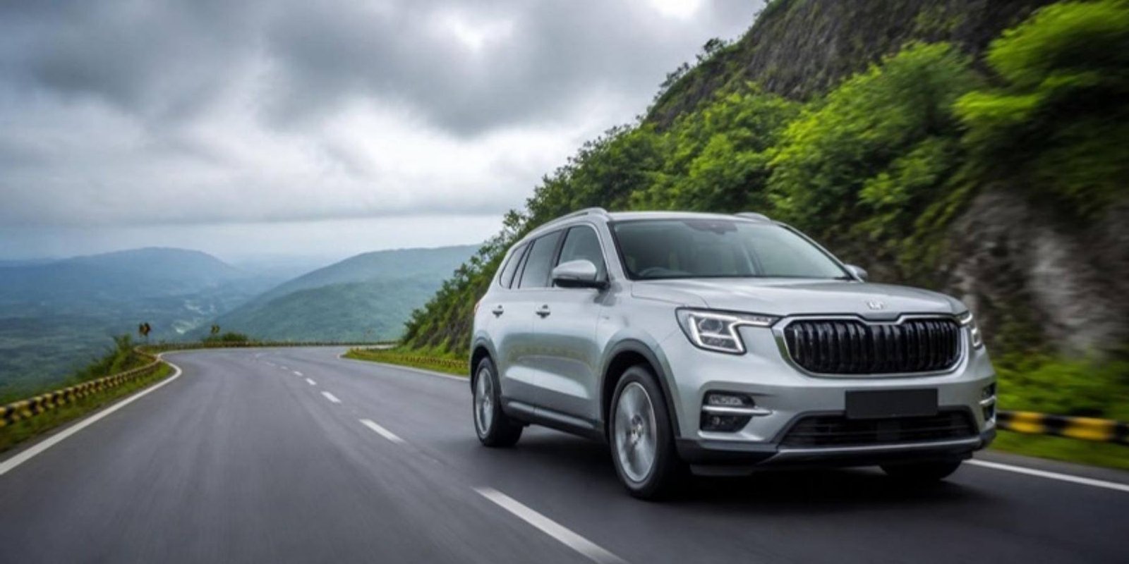 A silver family SUV driving on a green hill highway