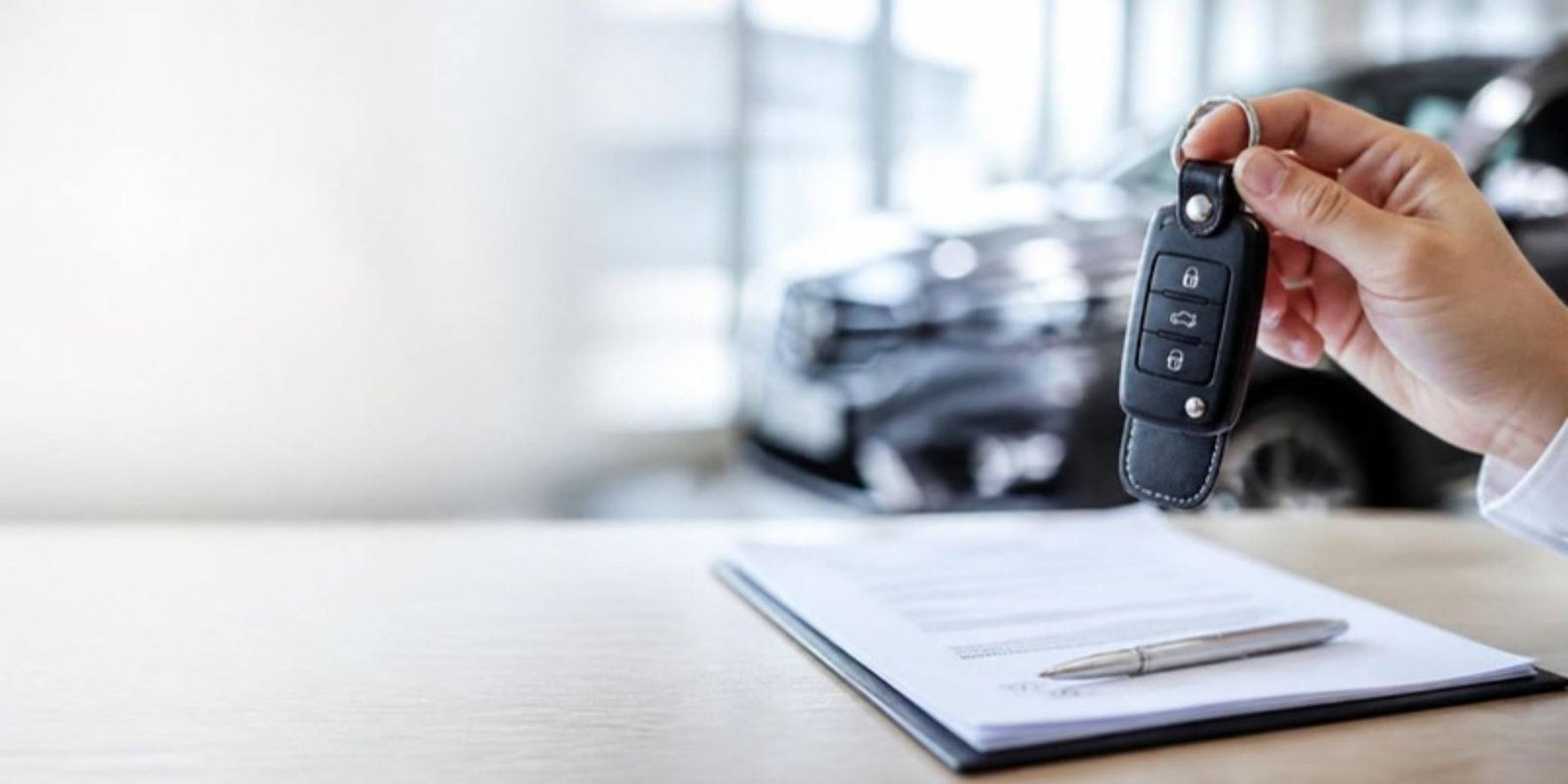 A new car key held above a signed loan document